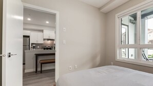 Un dormitorio con un ventanal grande, una puerta que da a un rincón americano y un banco.