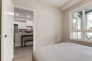 Une chambre dotée d’une grande fenêtre, d’une porte donnant sur un coin cuisine et d’un banc.