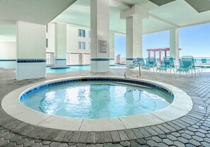 A pool area with a hot tub, lounge chairs, and a view of the ocean.