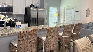A modern kitchen with white cabinets, stainless steel appliances, and a granite countertop. There are wicker chairs around the island and a gray sofa in the living area. - Amazing Townhouse Sleep10 Resort (Kissimmee)