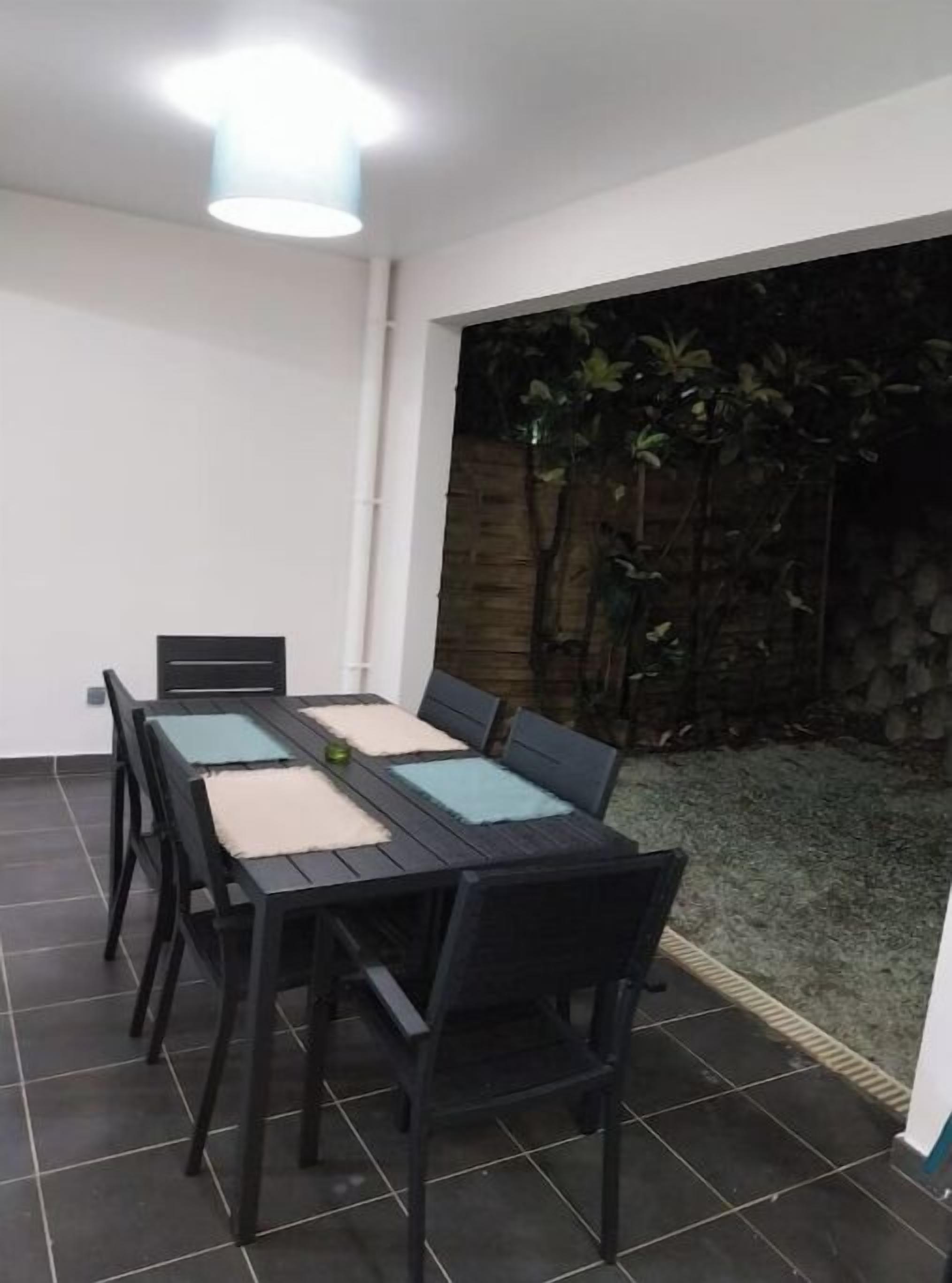 A dining area with a table and chairs, a ceiling light, and a view of a garden with plants.