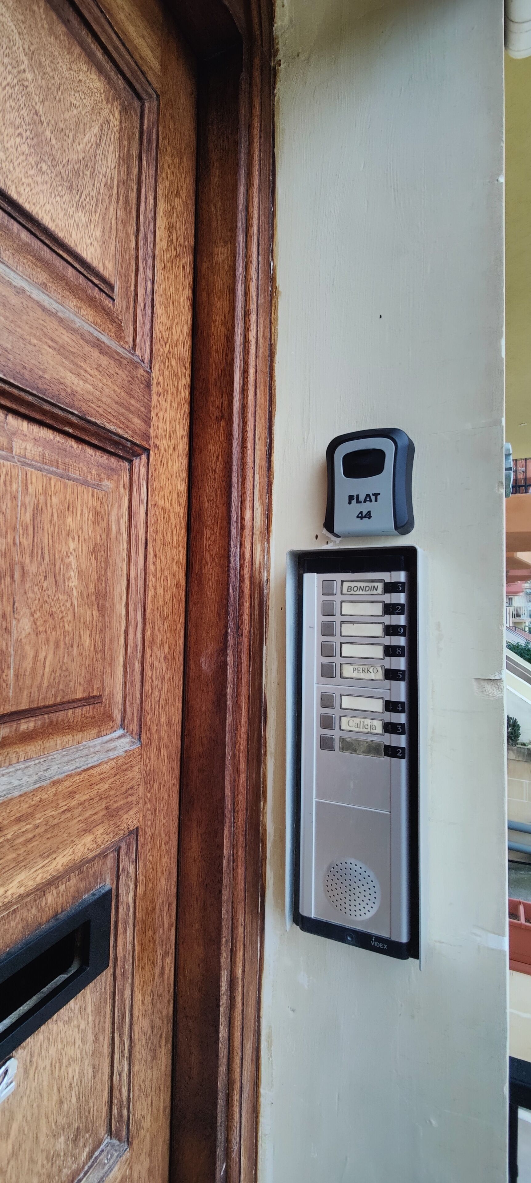 Une porte en bois, dotée d’un système d’interphone mural portant l’inscription « APPARTEMENT 44 » et d’un clavier à touches numériques.