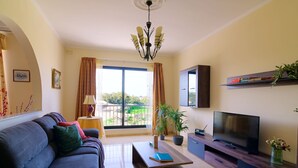 Una sala de estar con sofá, una mesa de centro, televisor y un balcón con cortinas.