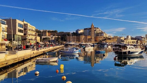 Un puerto deportivo con barcos amarrados, un paseo marítimo y edificios con balcones.