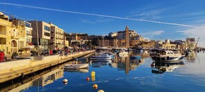 Un puerto deportivo con barcos amarrados, un paseo marítimo y edificios con balcones.