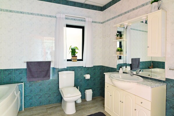 Un baño con inodoro, lavabo y bañera. Hay una ventana con una planta en el alféizar.