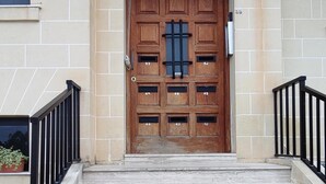 Entrada de un edificio con una puerta de madera que dice "Baja Vista", una escalera de piedra y una pequeña planta en maceta a la izquierda.