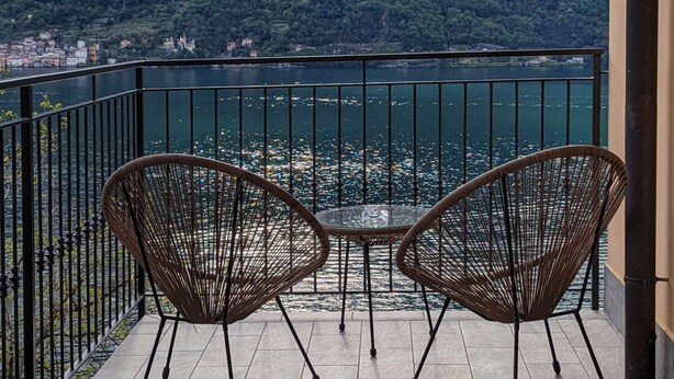 Un balcone con due sedie in vimini, pavimento piastrellato e vista su un lago e montagne.