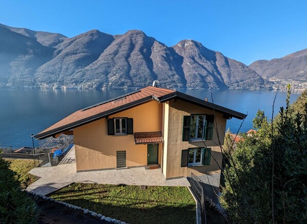 Ein zweistöckiges Haus mit Ziegeldach, einer Veranda und Blick auf einen See und Berge.