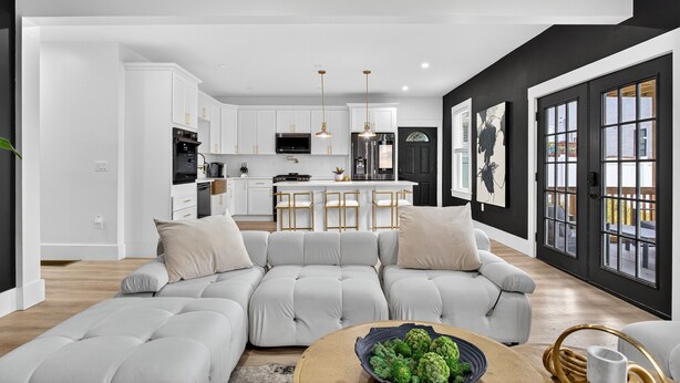 A modern living room with a sectional sofa, a coffee table with green plants, and a kitchen in the background. - Large victorian home 15 mins from downtown lots of local restaurants and bars  (Boston)