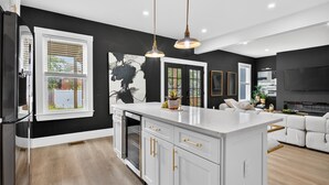 A modern kitchen with white cabinetry, a central island, pendant lighting, and a large black-and-white artwork. - Large victorian home 15 mins from downtown lots of local restaurants and bars  (Boston)