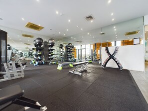 A modern gym with various exercise equipment, a large mirror, and a view of the city through large windows.