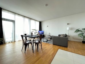 Uma sala de estar moderna com área de jantar, um sofá cinzento e uma televisão de tela plana.