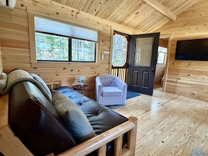 L’intérieur d’un chalet en bois, avec un canapé, un fauteuil et une porte donnant sur l’extérieur.
