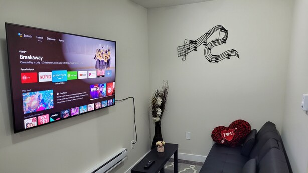 A living room with a flat-screen TV mounted on the wall displaying a streaming service interface. - Amazing 2 Bedroom  Suites. Very cozy and pet-friedly  (Saskatoon)