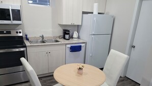 A compact kitchen with white cabinets, a stainless steel stove, a refrigerator, and a sink. There is a small table with a vase of flowers and two white chairs. - Amazing 2 Bedroom  Suites. Very cozy and pet-friedly  (Saskatoon)