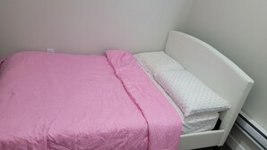 A small, white, single-bed room with a pink bedspread and a white pillow with a pattern. - Amazing 2 Bedroom  Suites. Very cozy and pet-friedly  (Saskatoon)