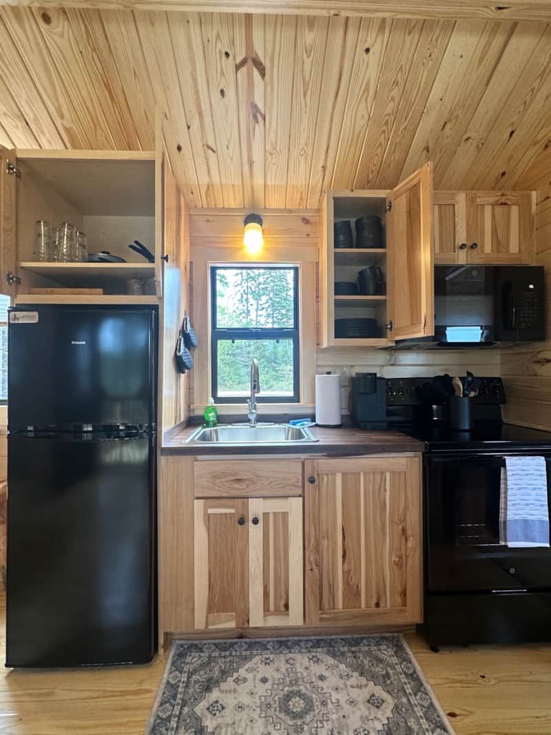 Una cocina compacta con armarios de madera, un refrigerador negro, un lavamanos y una estufa.