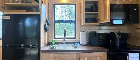 Una cocina compacta con armarios de madera, un refrigerador negro, un lavamanos y una estufa.