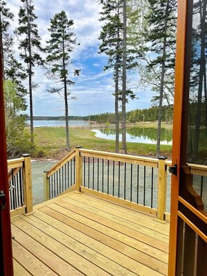 Una terraza de madera con barandilla, con vistas a un lago y un bosque.