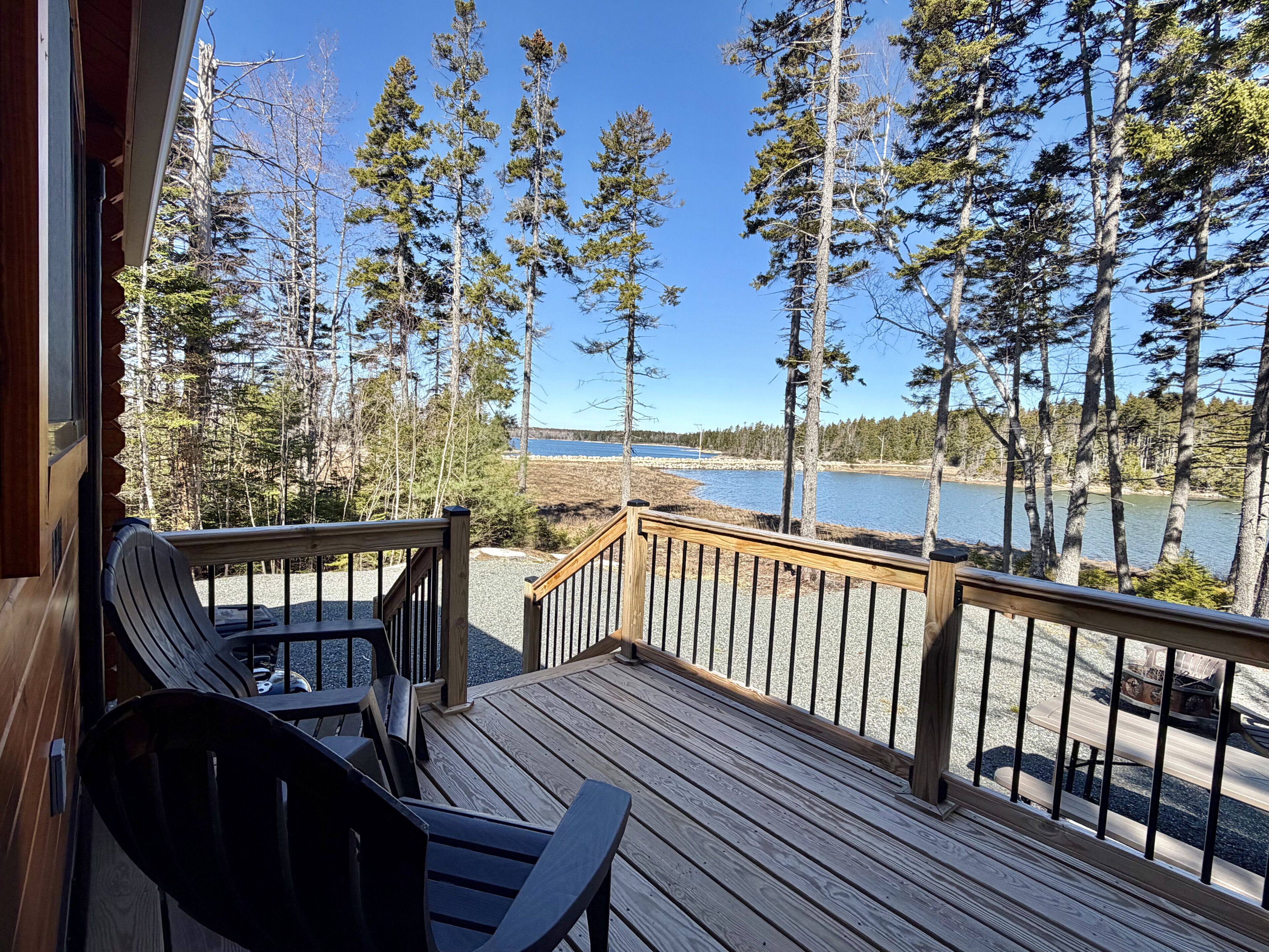 A wooden deck with chairs, a railing, and a view of a lake and forest.
