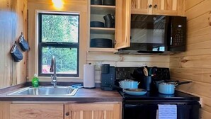 Une cuisine compacte avec des meubles en bois, un four à micro-ondes, une cuisinière et une fenêtre donnant sur un paysage verdoyant.