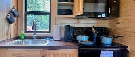 Une cuisine compacte avec des meubles en bois, un four à micro-ondes, une cuisinière et une fenêtre donnant sur un paysage verdoyant.