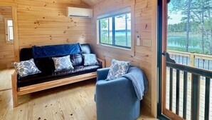 L’intérieur chaleureux d’un chalet avec un plafond en bois, un canapé, un fauteuil et une grande fenêtre donnant sur le paysage extérieur.