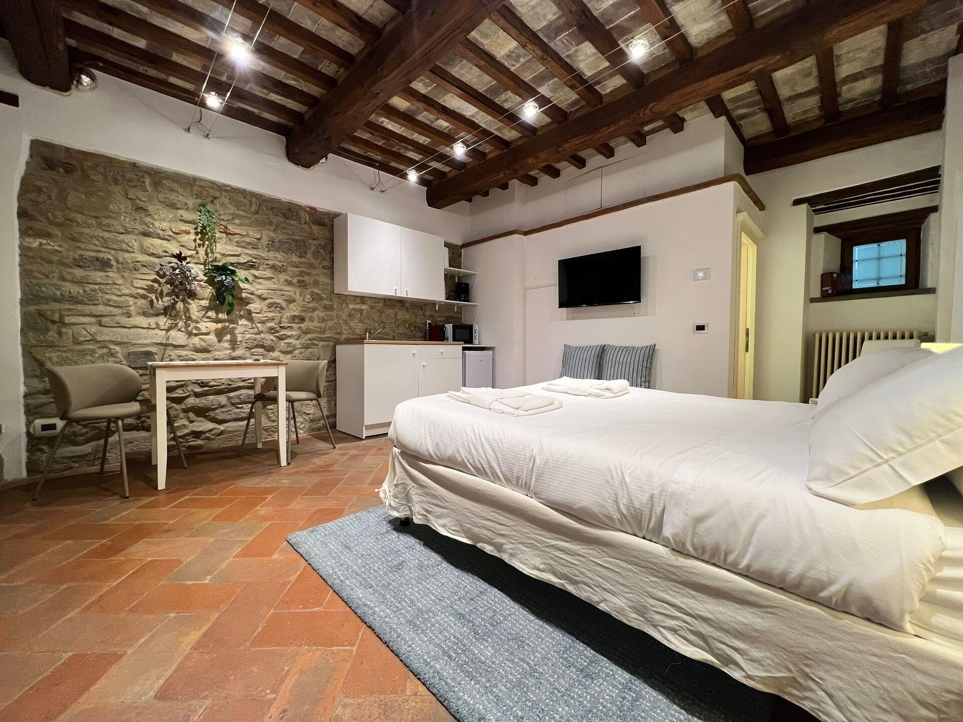 A bedroom with a stone wall, a bed, a desk, and a television.