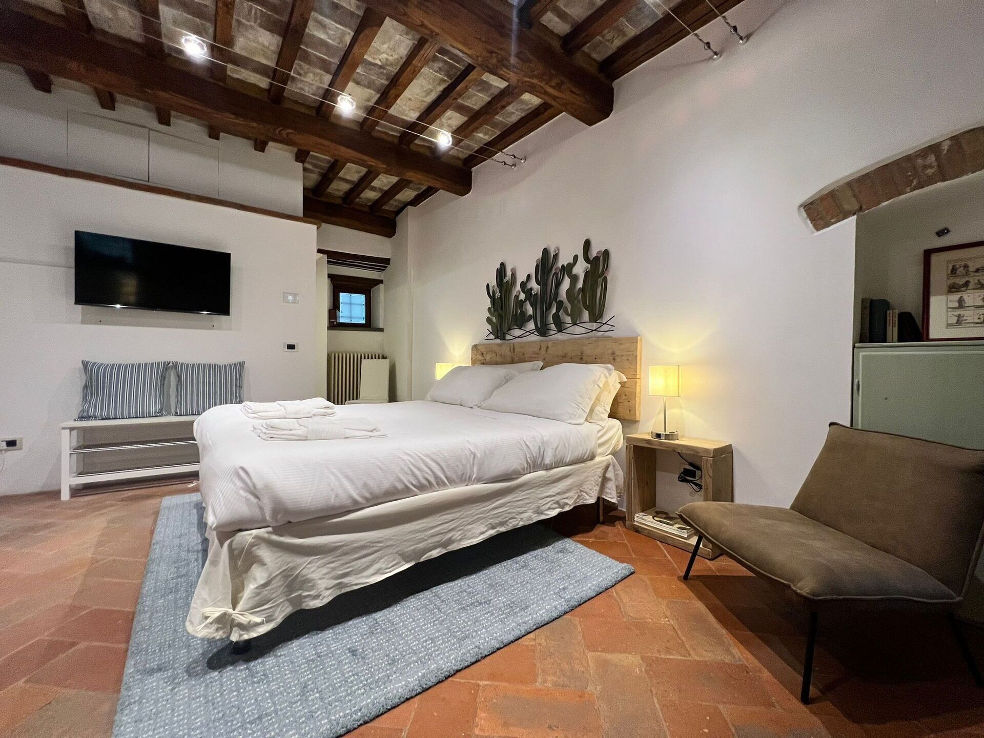 Un dormitorio con una cama, televisión, decoración de pared con cactus y un banco.