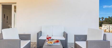 Un patio con mobiliario de mimbre, una mesa con comida y bebidas, y vistas al exterior.