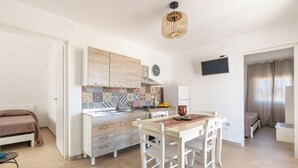 A modern kitchen with a dining area, a TV mounted on the wall, and a clock.