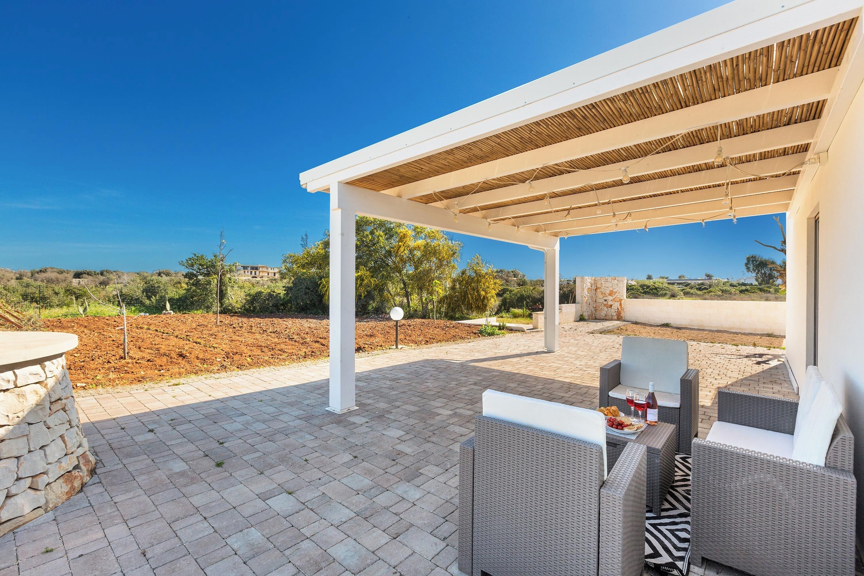 An outdoor patio area with wicker furniture, a stone table, and a pergola structure.