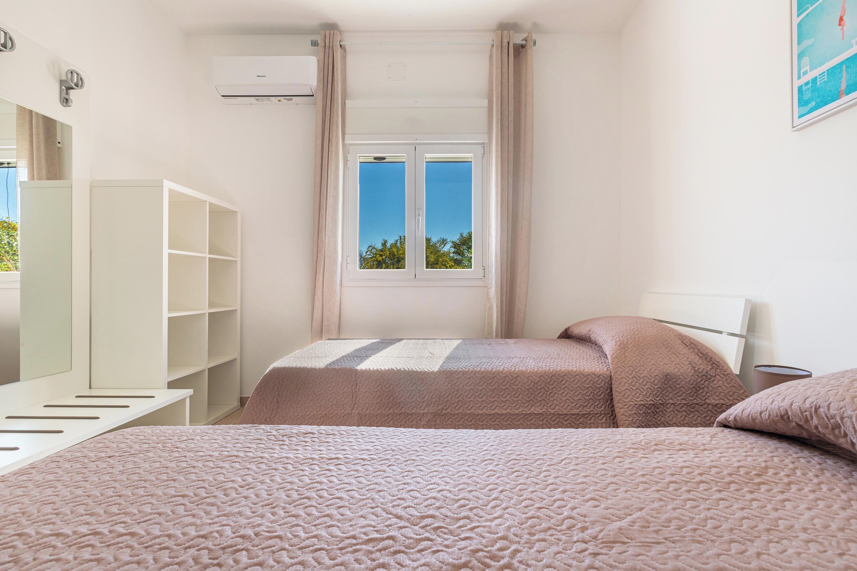 A bedroom with a bed, a wardrobe, a window with curtains, and an air conditioning unit.