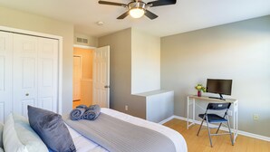 Un dormitorio con cama, almohadas, un escritorio con silla, un televisor y un ventilador de techo.