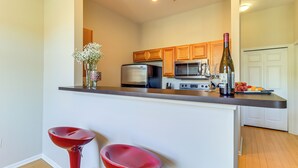 Una cocina con armarios de madera, un refrigerador de acero inoxidable, un microondas y una botella de vino sobre la encimera.