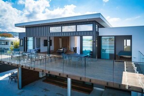 A modern building with a glass balcony, a wooden deck, and a view of the water.