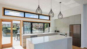 A modern kitchen with a large island, stainless steel appliances, and pendant lighting. - SouthWind (Merimbula)