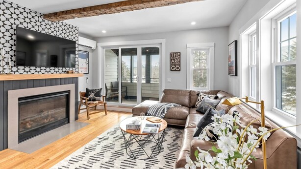 A modern living room with a fireplace, a large TV, and a cozy seating area with a sofa and chairs. - Bearfoot Lodge (Waterville Valley)