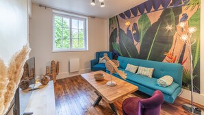 A modern living room with a blue sofa, a wooden coffee table, and a large tropical mural on the wall. - Le Jungle - Appt pour 6 avec parking privé (Paray-le-Monial)