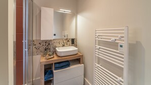 A bathroom with a white sink, a mirror, a towel rack, and a shower area. - Le Jungle - Appt pour 6 avec parking privé (Paray-le-Monial)
