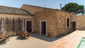 A stone building with a tiled roof, a wooden table with chairs, and a tiled patio area.