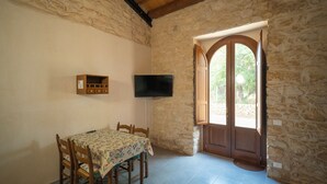 A dining area with a table and chairs, a television mounted on the wall, and a stone wall with a wooden door.