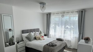 Ein modernes Schlafzimmer mit einem großen Bett, einem Nachttisch, einer Kommode, einem Spiegel und einer Pendelleuchte.