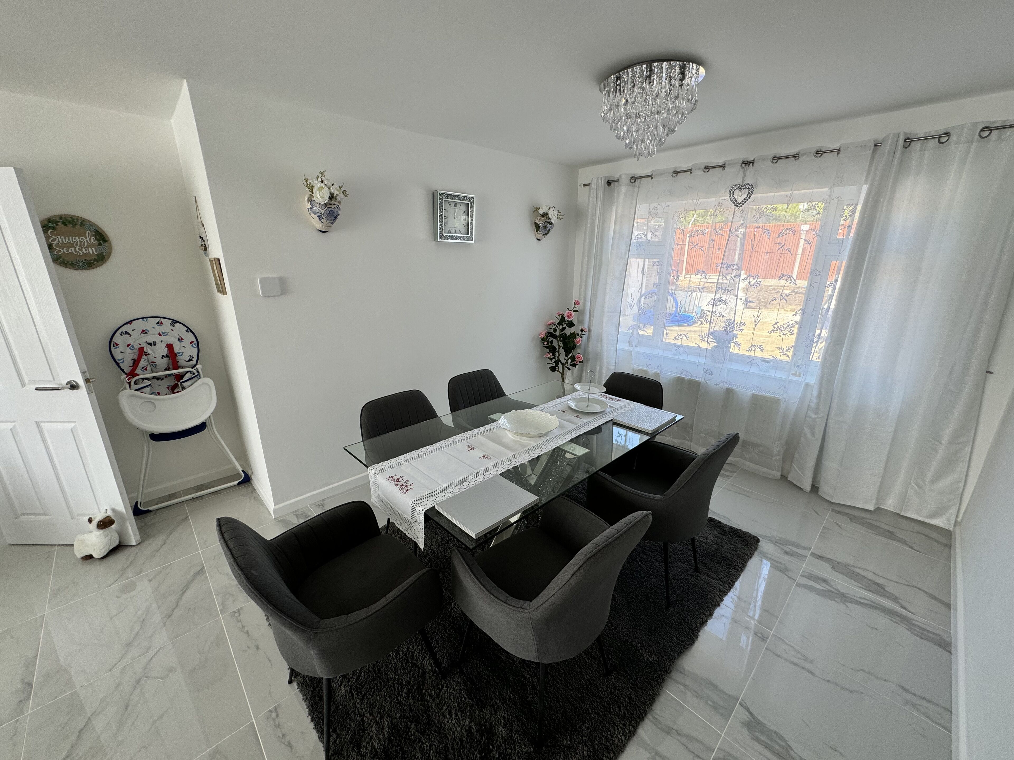 A dining area with a glass table, black chairs, a chandelier, and a view of the outside.