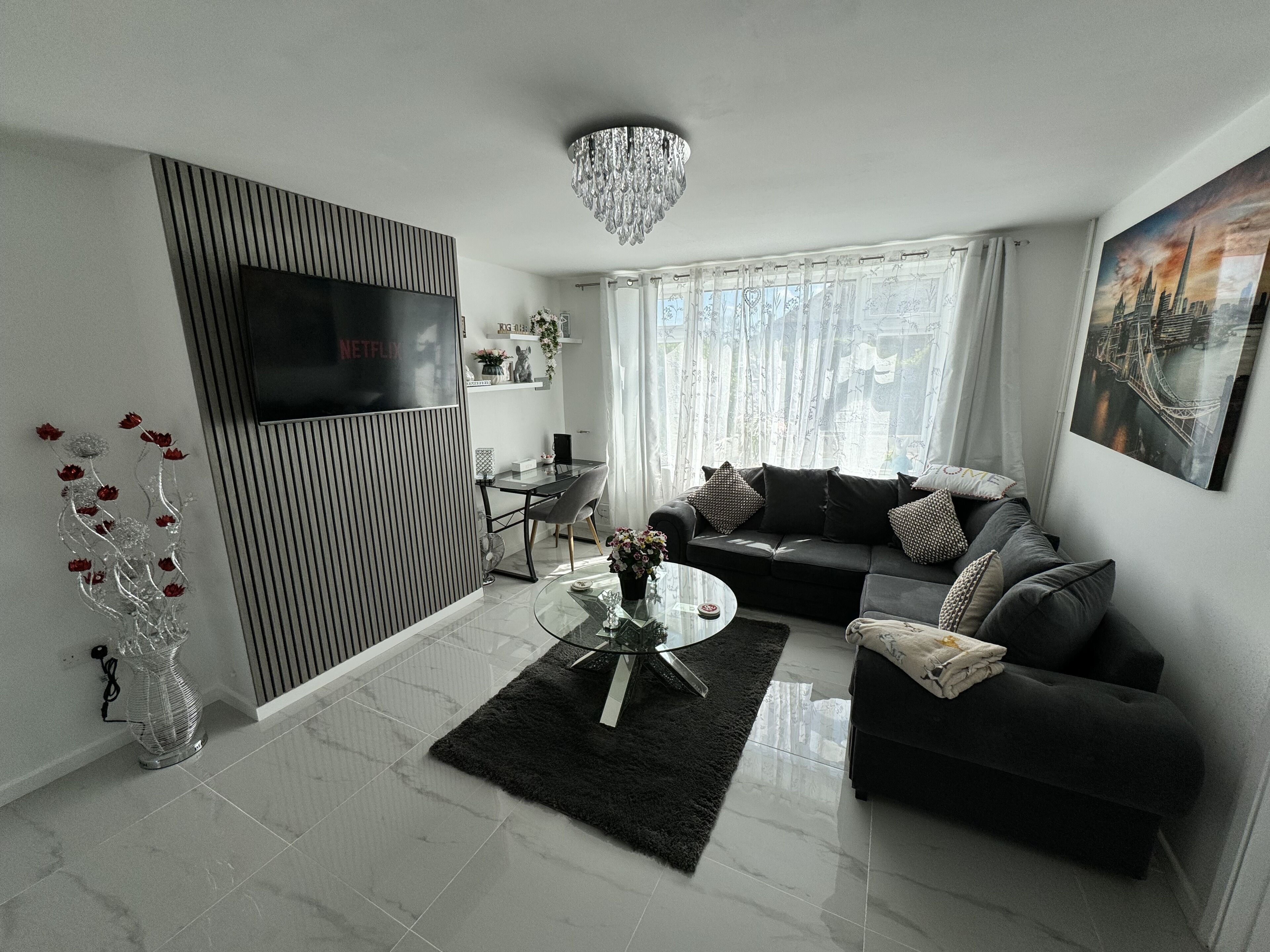 A modern living room with a flat-screen TV, a sofa, a glass coffee table, and a chandelier.