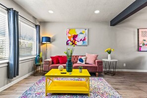 A living room with a sofa, a yellow coffee table, a floor lamp, and artwork on the walls.