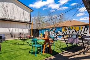 An outdoor patio with a mural, green artificial grass, and outdoor furniture.