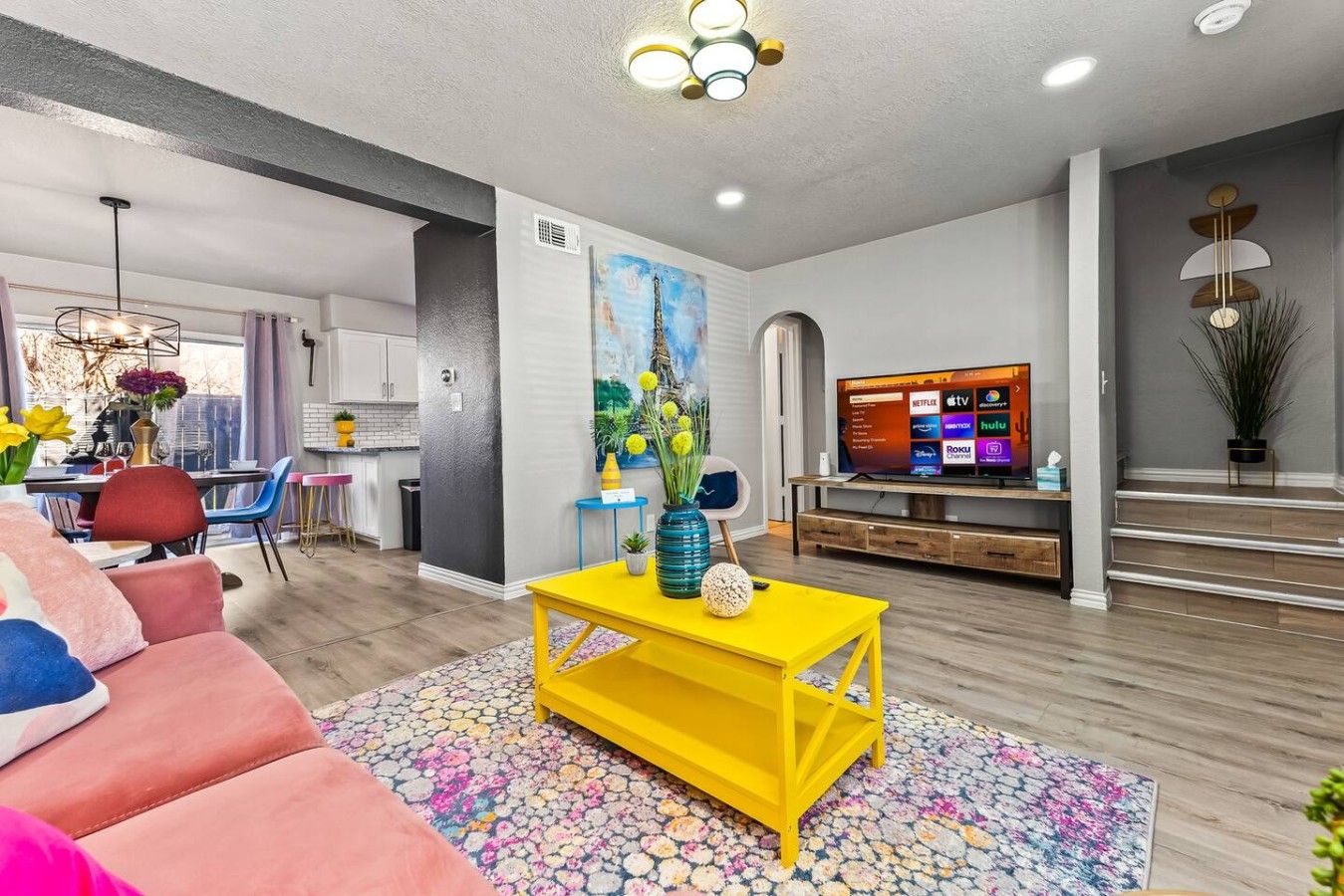 A modern living room with a yellow coffee table, a television, and a dining area with a table and chairs.