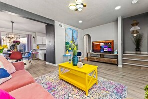 A modern living room with a yellow coffee table, a television, and a dining area with a table and chairs.